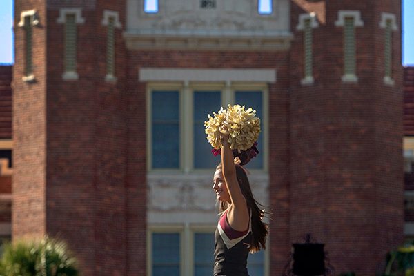 A Florida State University cheerleader is held in the air with the Westcott building as a backdrop during the annual Homecoming Parade.
