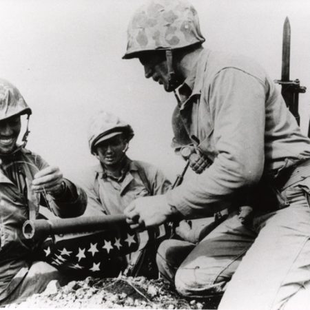 Ernest “Boots” Thomas, a former resident of North Florida, ties the first flag to a pipe that would be used as flag pole for the first American flag raised in Iwo Jima. Marines from 3rd Platoon, Company E, 2nd Battalion, 28th Marine Regiment raised a fifty-four by twenty-eight inch flag during the Battle of Iwo Jima. Because this flag proved too small to clearly see from the ground 546 feet below, a second flag measuring eight by four feet replaced the first one that is now famously depicted in Joe Rosenthal’s photograph.
