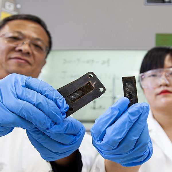 Professor Zhiyong (Richard) Liang and research faculty member Ayou Hao holding pieces of carbon fiber reinforced polymer composites coated with a protective heat shield made of a carbon nanotube sheet that was heated to a temperature of 1,900 degrees Celsius.