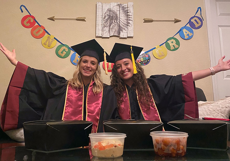 Ashley Sanders and her roommate, Melissa Beale, wear their caps and gowns as they watch virtual commencement and enjoy curbside pick-up from Madison Social. (Ashley Sanders)