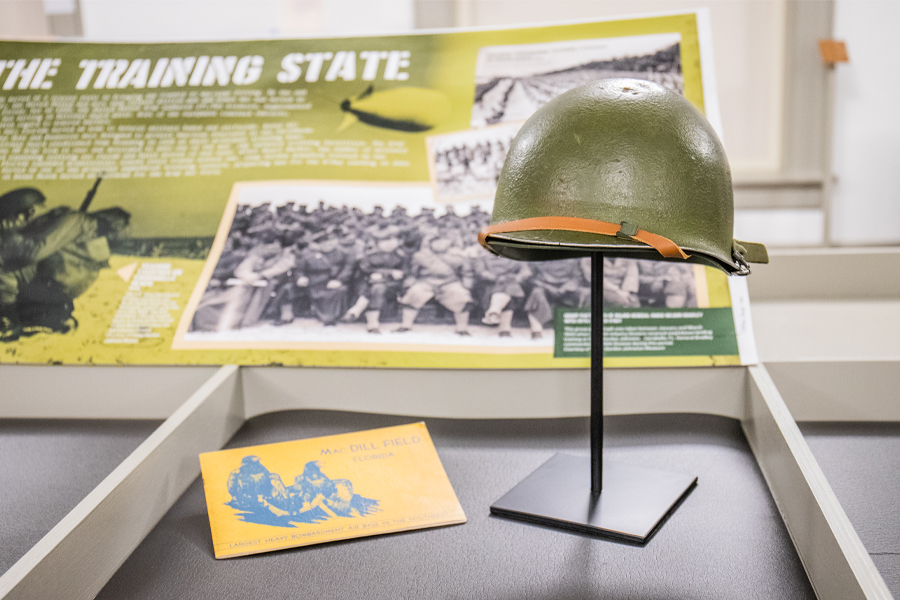 The exhibit includes artifacts such as a brochure loaned by the Tampa Bay History Center about MacDill Field, which was built near Tampa in 1939 and was critical in defending the Gulf of Mexico against Nazi U-boat attacks on merchant ships. To the right is an M1 helmet loaned from Camp Blanding Museum. The U.S. Army designed the manganese steel M1 helmet and started production in April 1941. Over 22 million of these helmets were produced during World War II. (Photo courtesy of Florida Historic Capitol Museum)