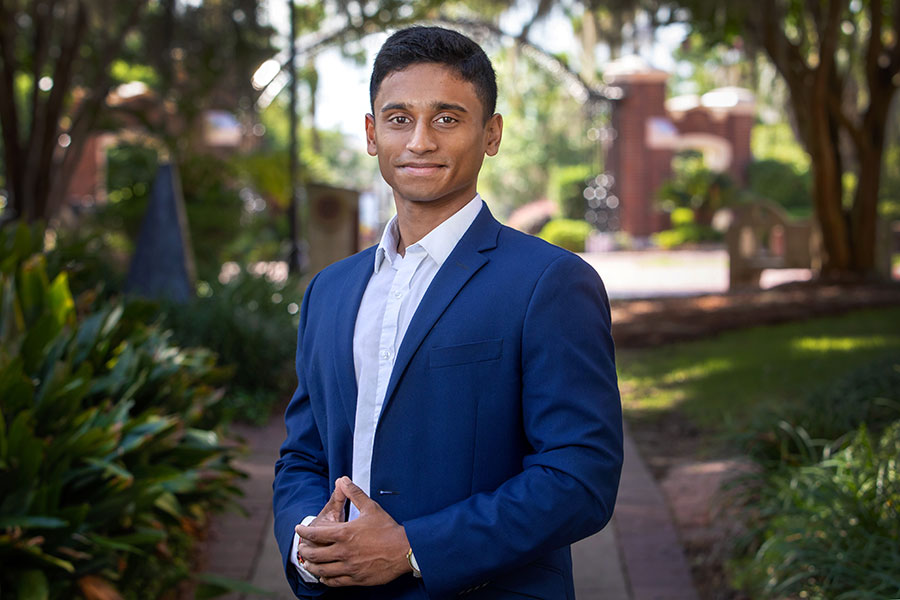 Headshot of FSU Student Body President Nimna Gabadage, who has been elected to serve as Chair of the Florida Student Association. He is posing outside near Wescott Fountain and wearing a blue suit, with his hands clasped in front of him. 