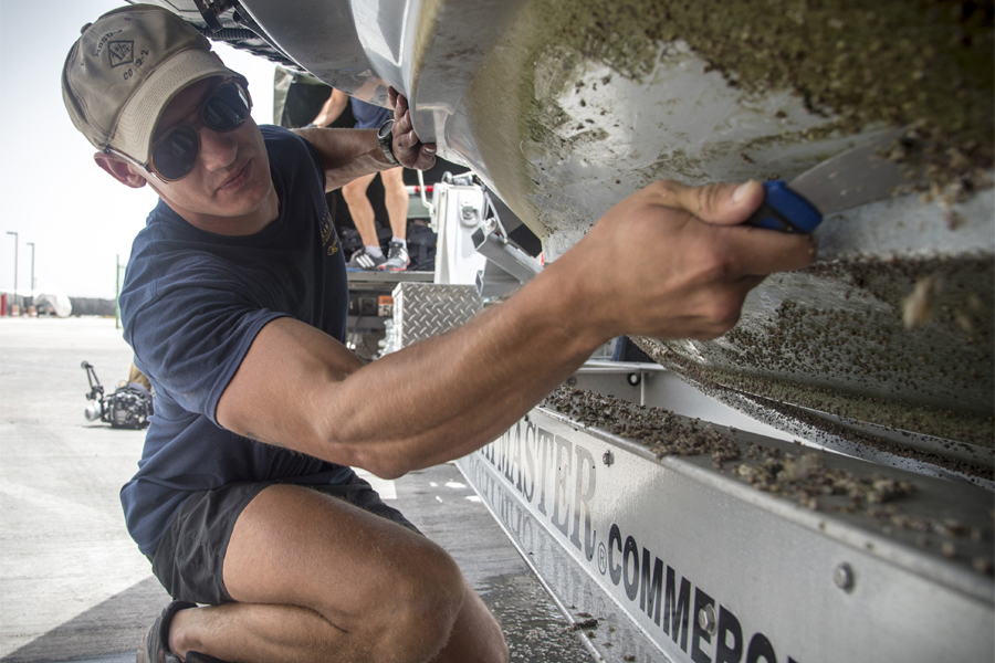 Navy Diver 2nd Class Camden Lund scrapes barnacles from the bottom of a rigid-hull inflatable boat. (U.S. Navy photo by Mass Communication Specialist 3rd Class Wyatt Huggett/Released)