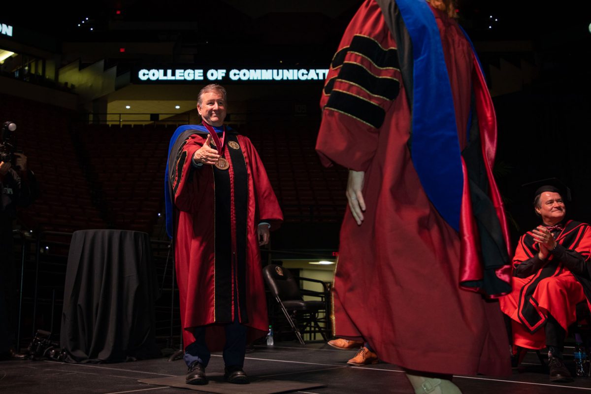 Florida State University President Richard McCullough reaches out to shake a graduate's hand during the summer doctoral hooding ceremony Friday, Aug. 4, 2023, at the Donald L. Tucker Civic Center. (FSU Photography)
