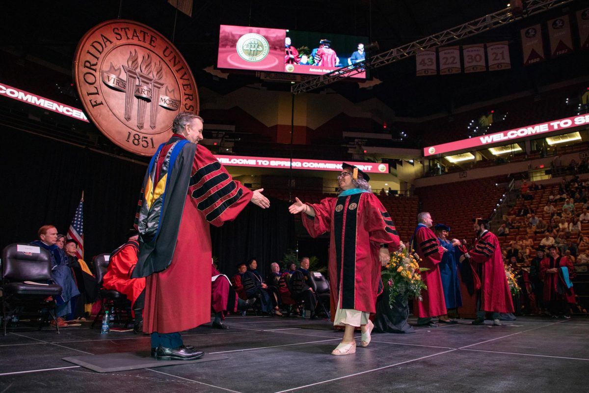 FSU President Richard McCullough reaches out to shake a graduate's hand during the spring doctoral hooding ceremony Friday, May 3, 2024, at the Donald L. Tucker Civic Center. (FSU Photography)