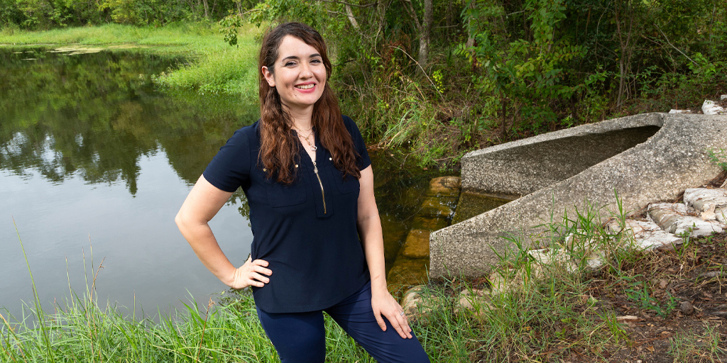 A photo portrait of Nasrin Alamdari standing in front of a creek and sewage pipe.