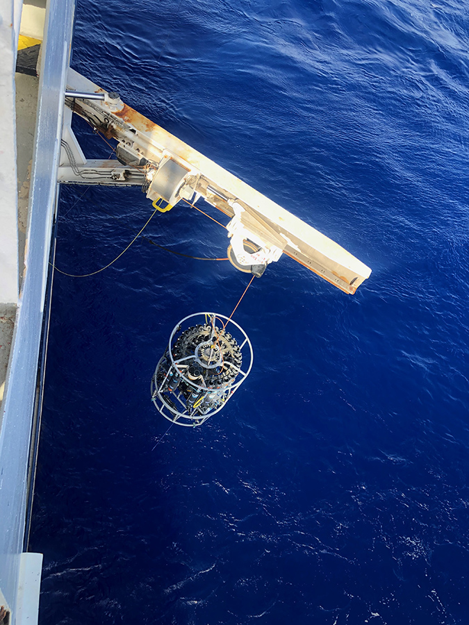 A hoist on a ship pulls up a device for sampling sediment from the ocean.