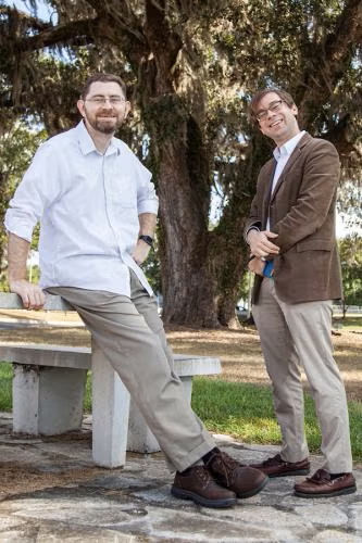 Two men stand in front of a large live oak tree.