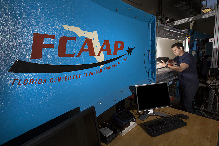 An engineering laboratory. A man works in the background. In the foreground is a piece of machinery painted blue with the logo for the Florida Center for Advanced Aero-Propulsion.