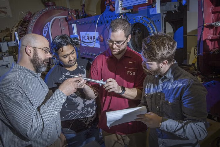 A group of researchers examining a rocket prototype in an engineering laboratory.