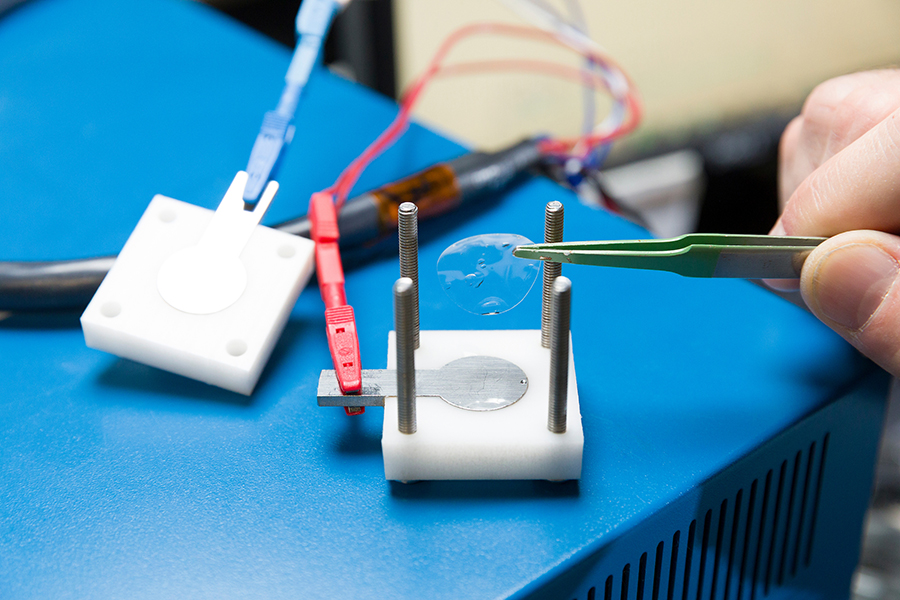 Tweezers holding a thin, transparent membrane above a testing device.