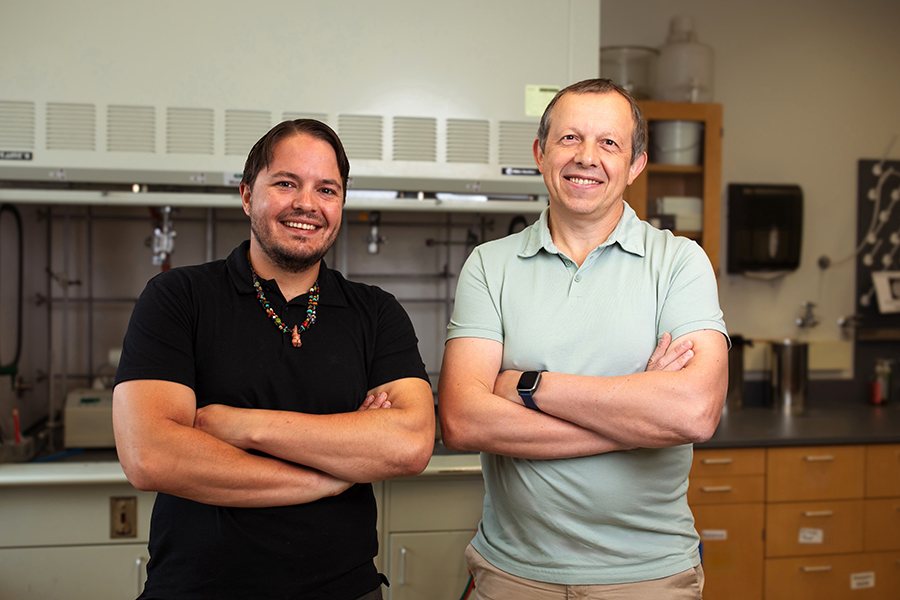 Two men stand with arms crossed in a chemistry lab.