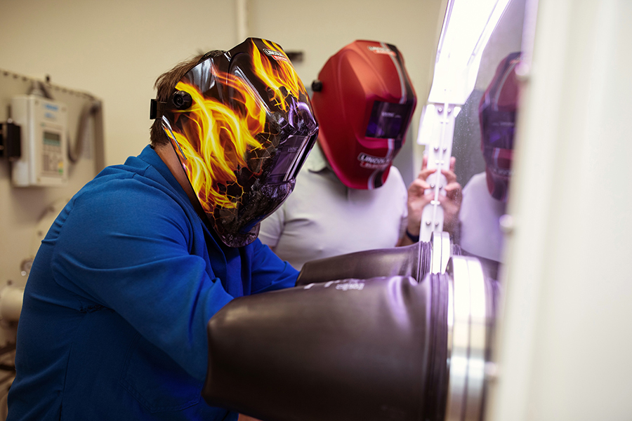 Two people wearing welding helmets working in a chemistry laboratory.
