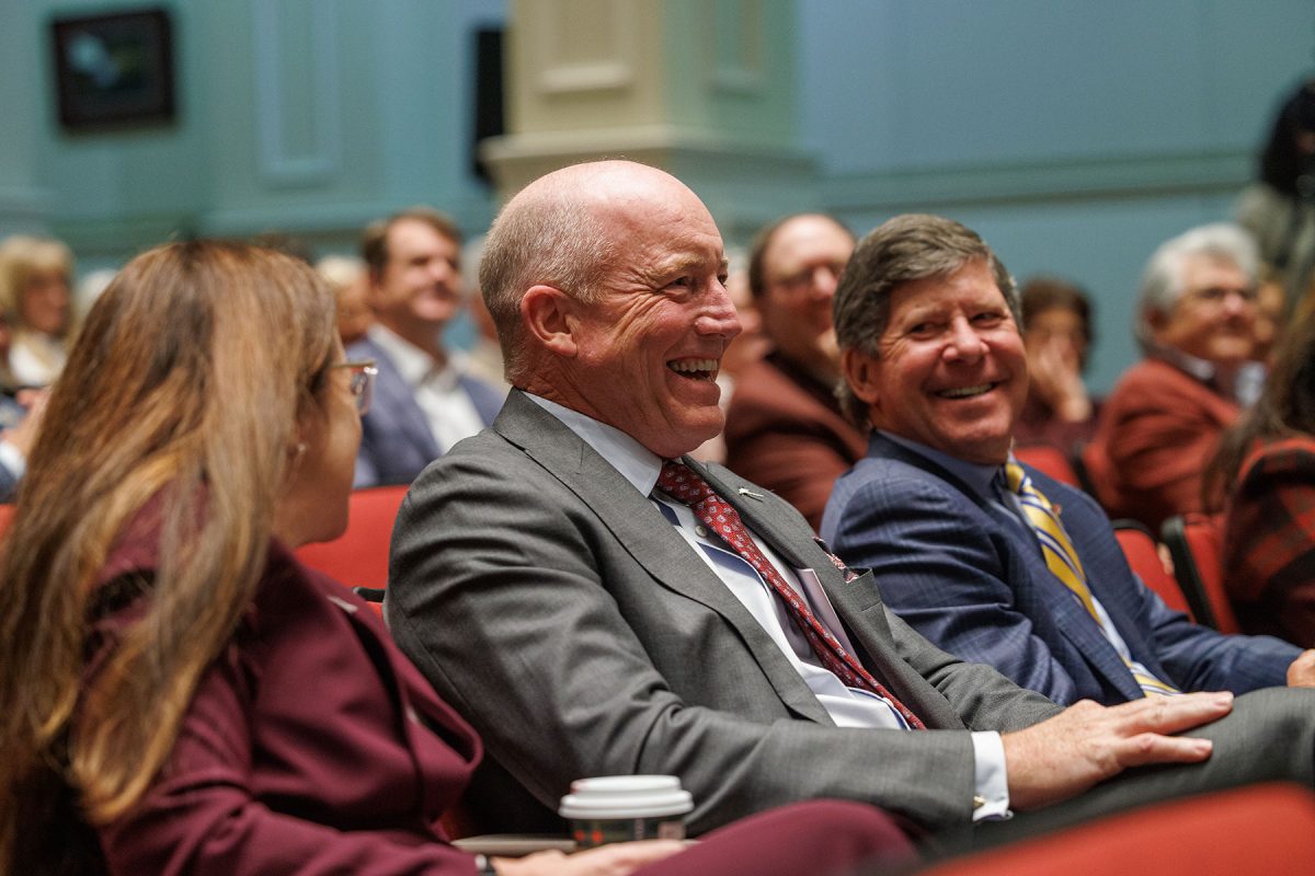 Two men in suits share a laugh at an auditorium.