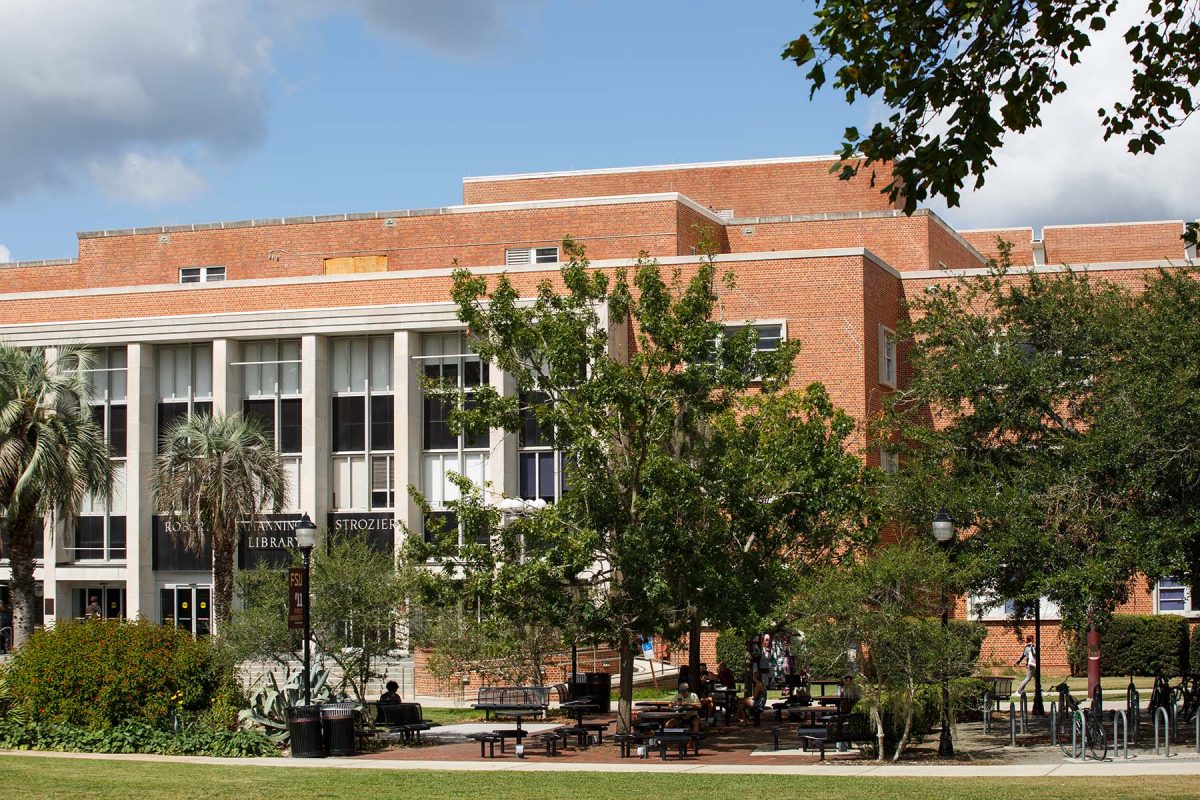 Exterior view of Florida State University’s Strozier Library on a sunny day, with brick walls, tall white columns, and trees and seating areas in the foreground.