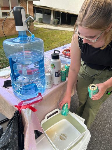 A student rinsing out aluminum cans at a sustainable film set beverage station to prepare them for recycling.
