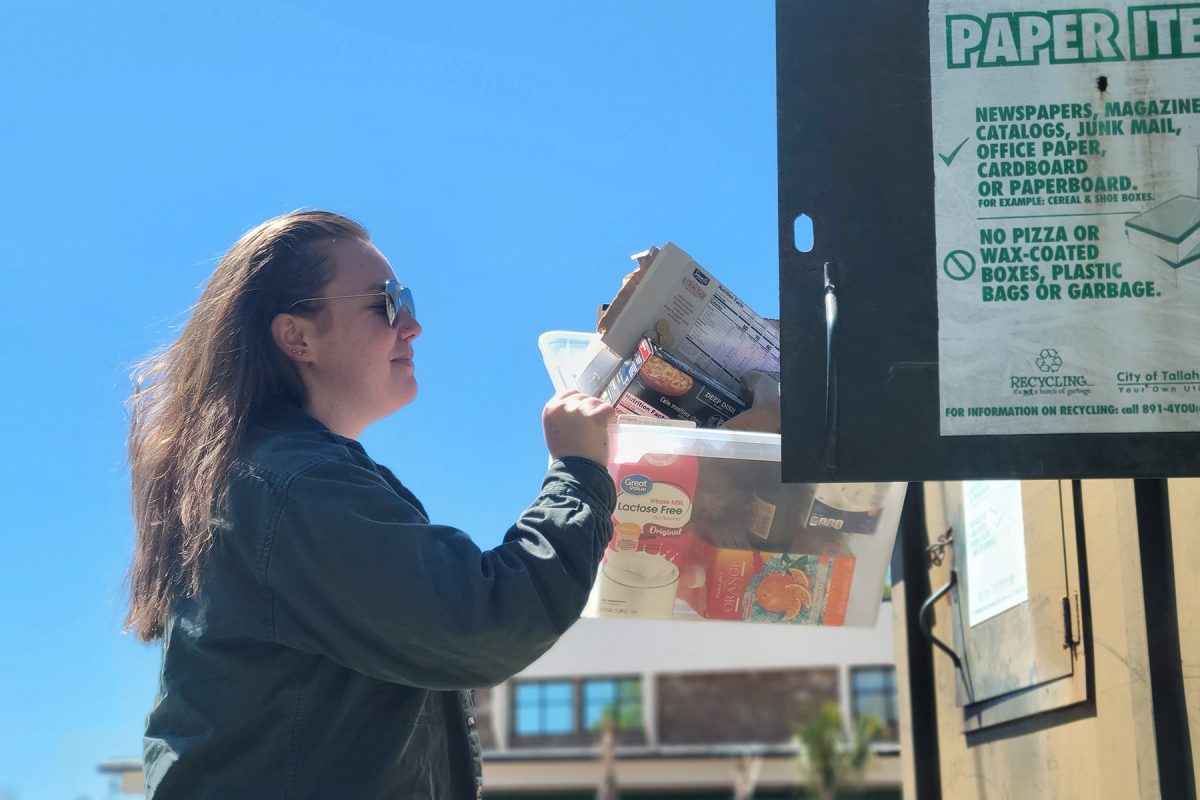 Close-up of a Tallahassee city recycling bin for paper products, showing a person emptying a bin of assorted cardboard packaging.