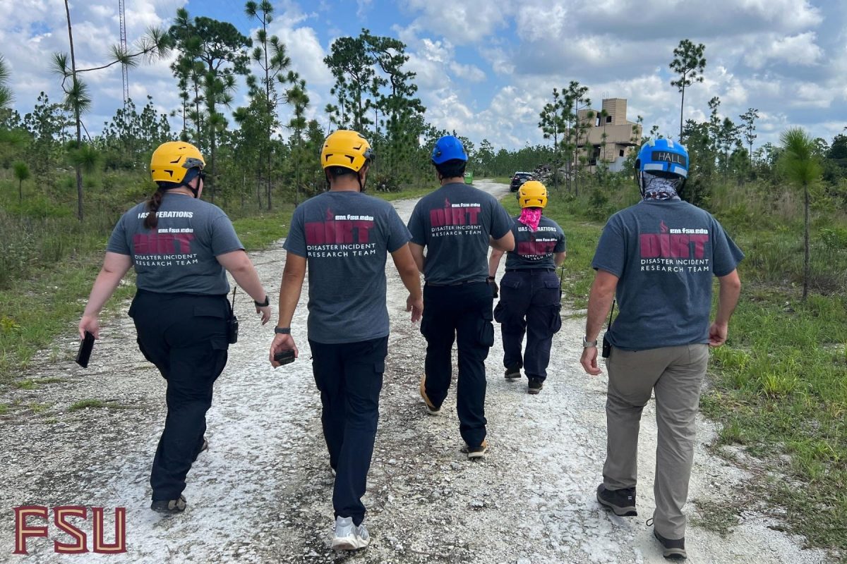 Emergency management students wearing helmets walk through a rural field on a gravel path