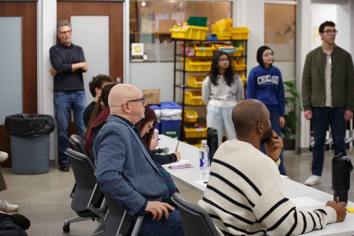A panel of four judges sit at a table and look forward.