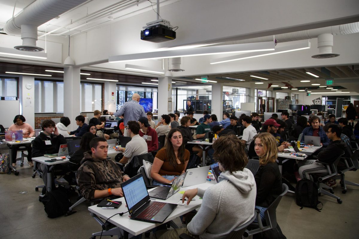 Many students sit at different tables and talk to one another.