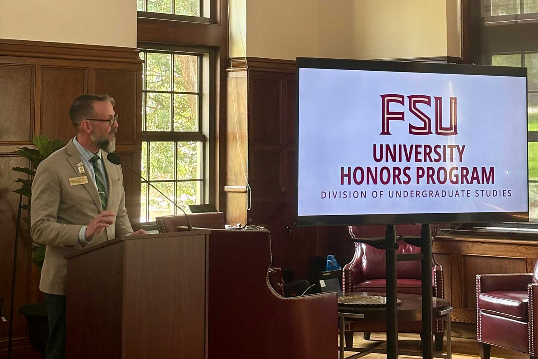 Craig Filar, Associate Dean of Honors, Scholars, and Fellows, speaks at a wooden podium during the Honors in the Major Faculty Appreciation Reception.
