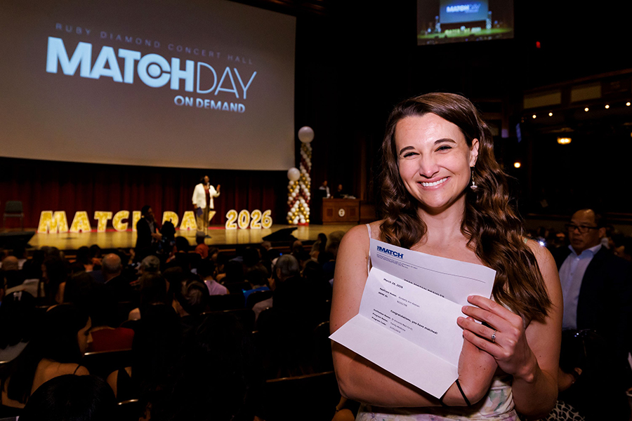 A woman smiles as she holds up information showing where she match for a medical residency program.