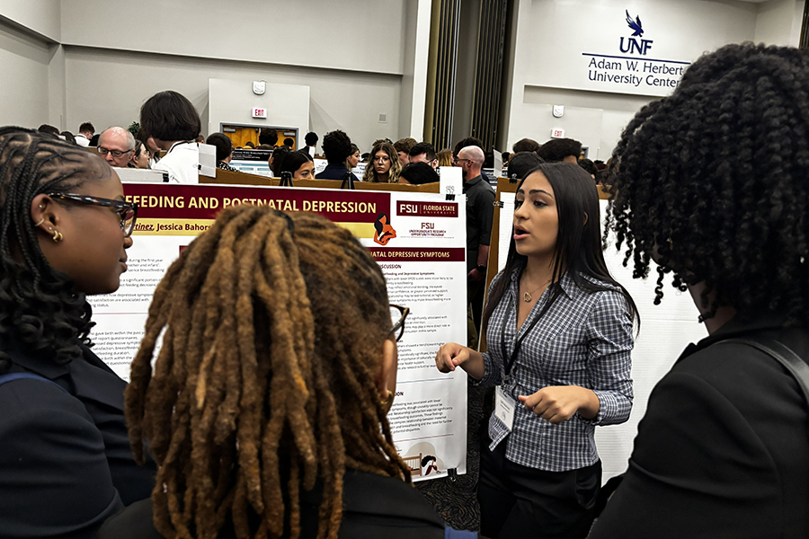 A woman speaks to a group of three people in front of a research poster.