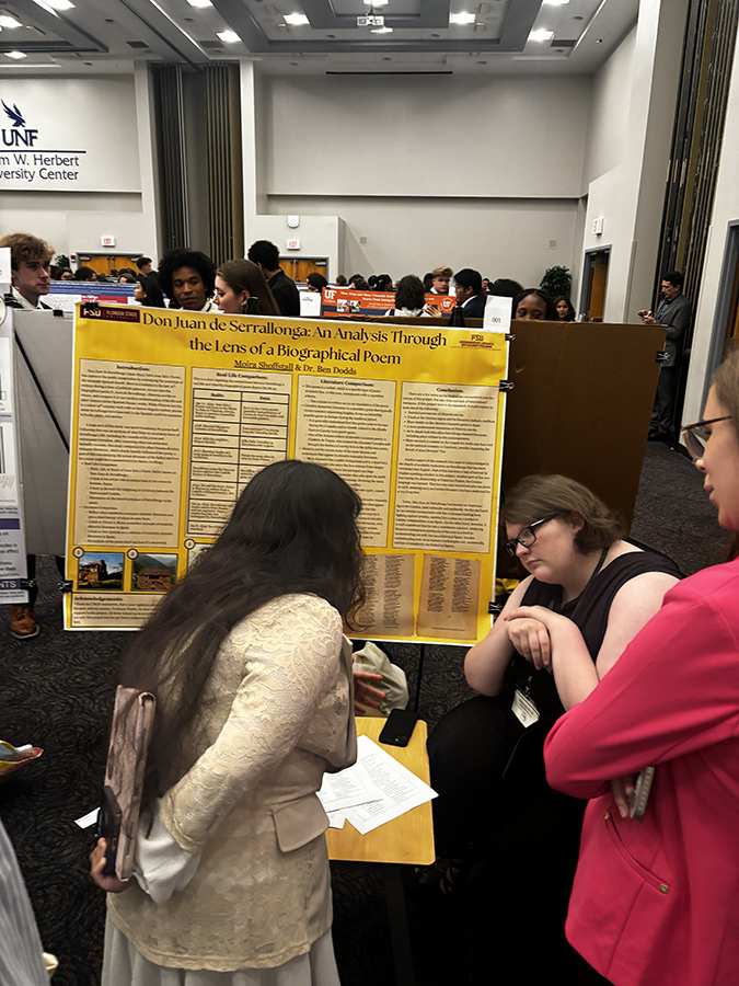 A woman speaks to another person in front of a research poster.