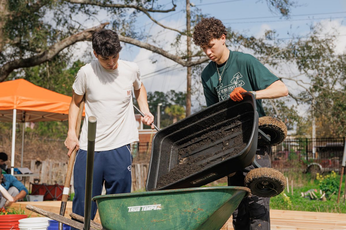 A young man lifts dirt into a green wheelbarrow