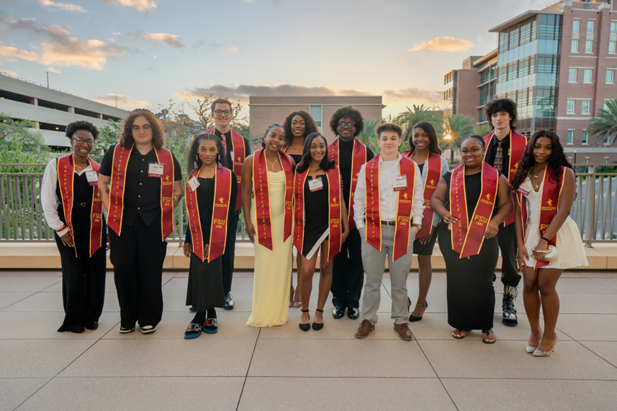 Group of students with garnet and gold sashes posing outside on the Student Union patio.