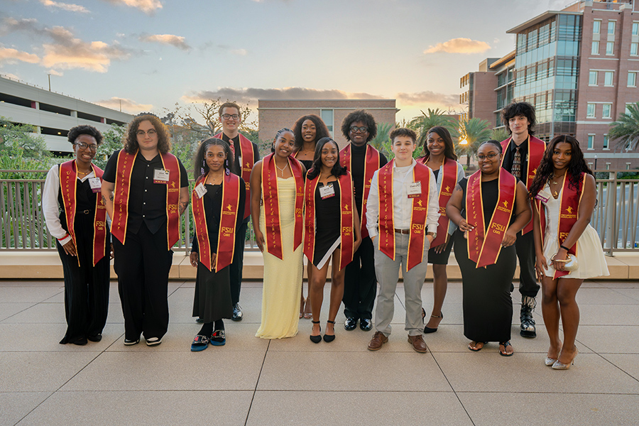 Group of students with garnet and gold sashes posing outside on the Student Union patio.