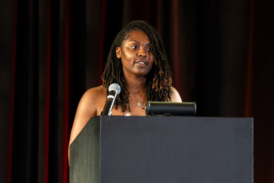 Black woman with long hair speaking at podium.
