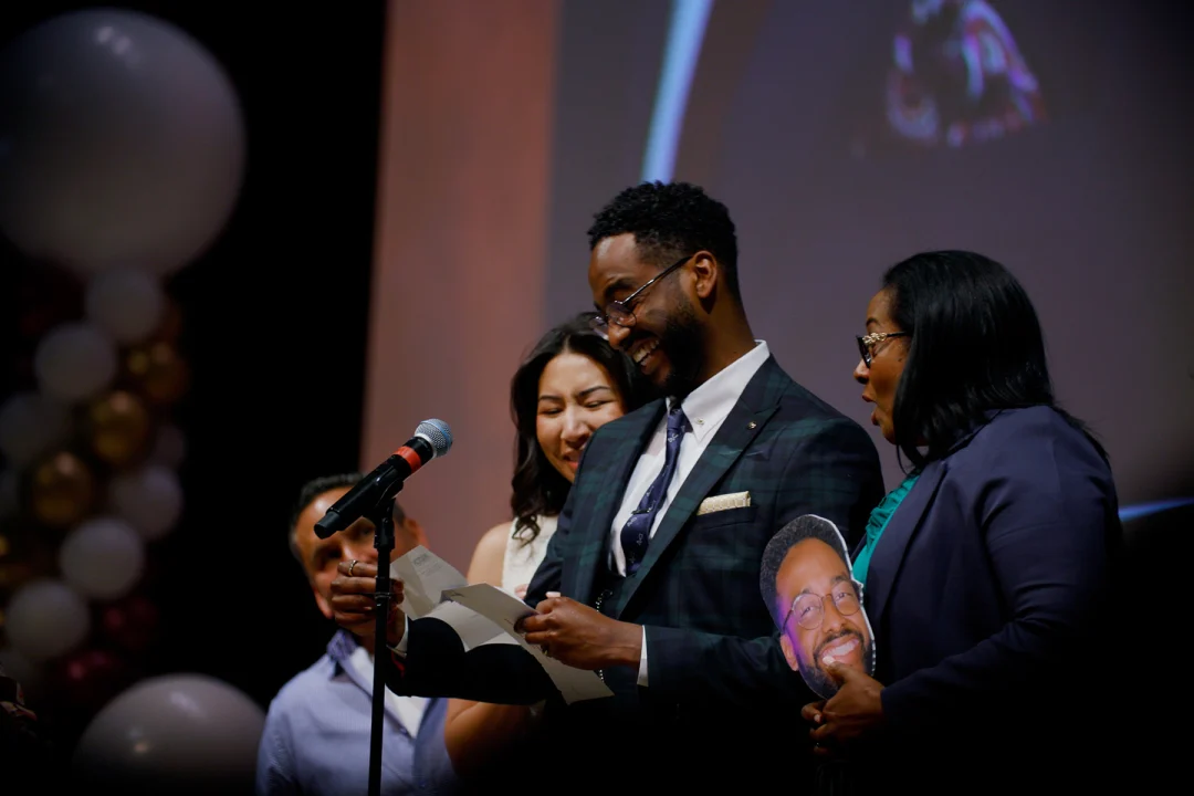 People look at a piece of paper with shock and delight, standing in front of a microphone
