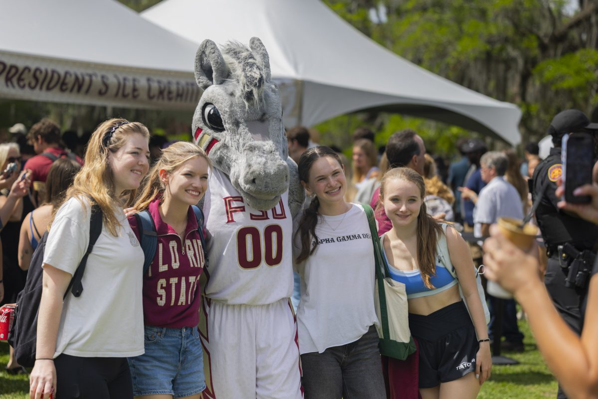 Four students smile and pose with a mascot for a photo being taken on a phone