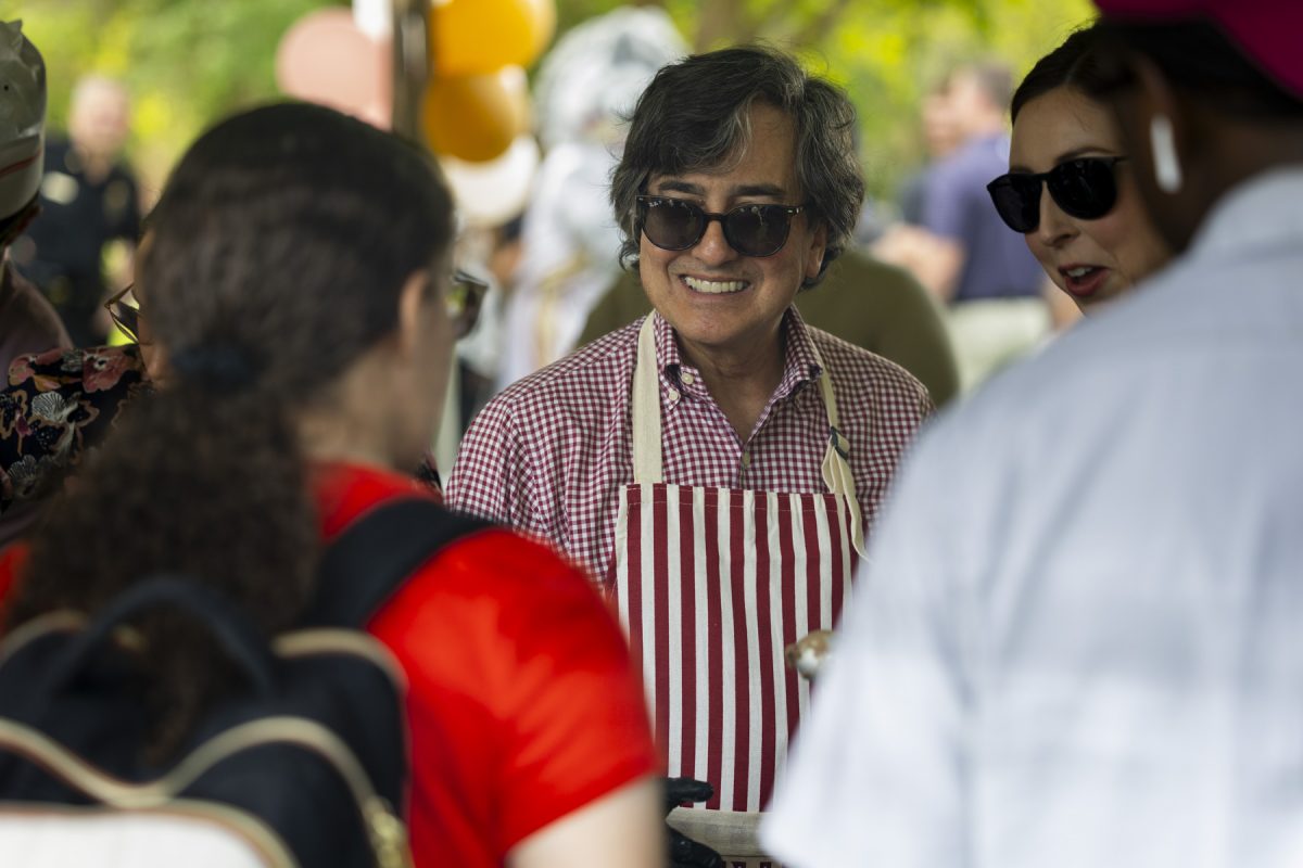 A man in sunglasses and a red and white striped apron smiles and looks forward to someone
