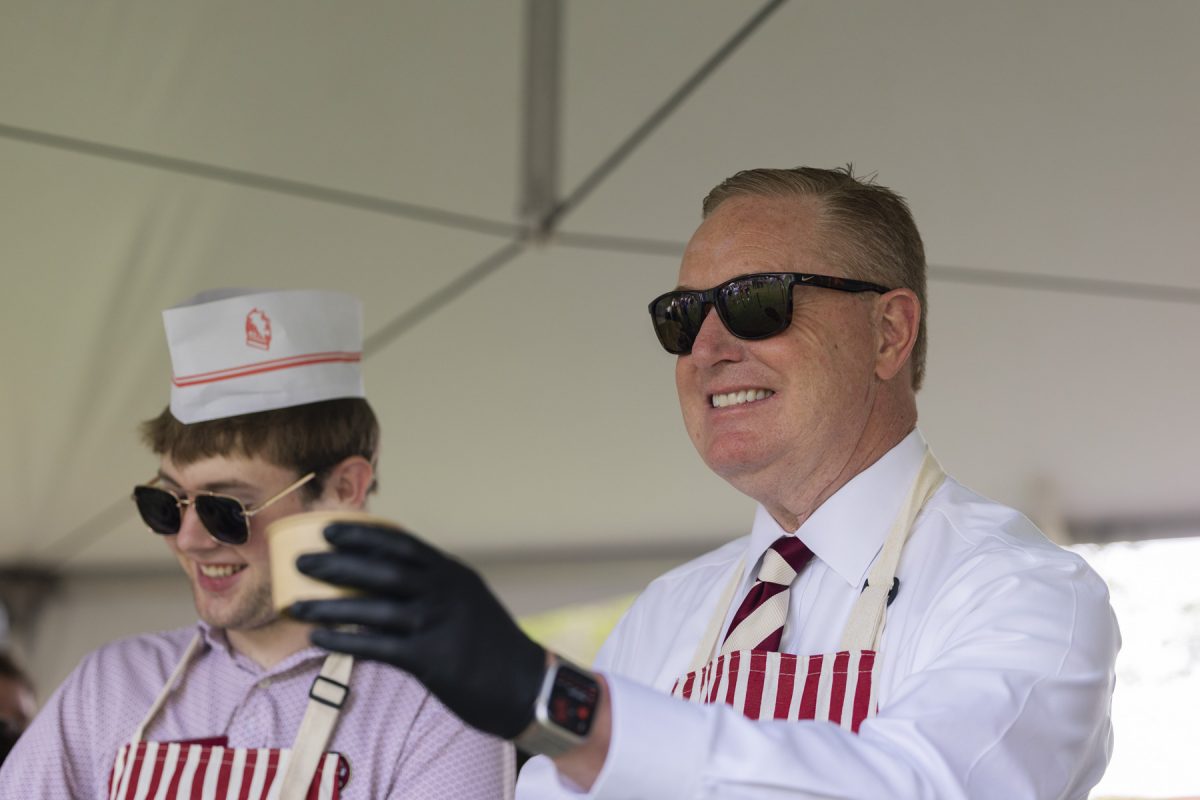 Two men wearing sunglasses smile, one more in focus looking forward