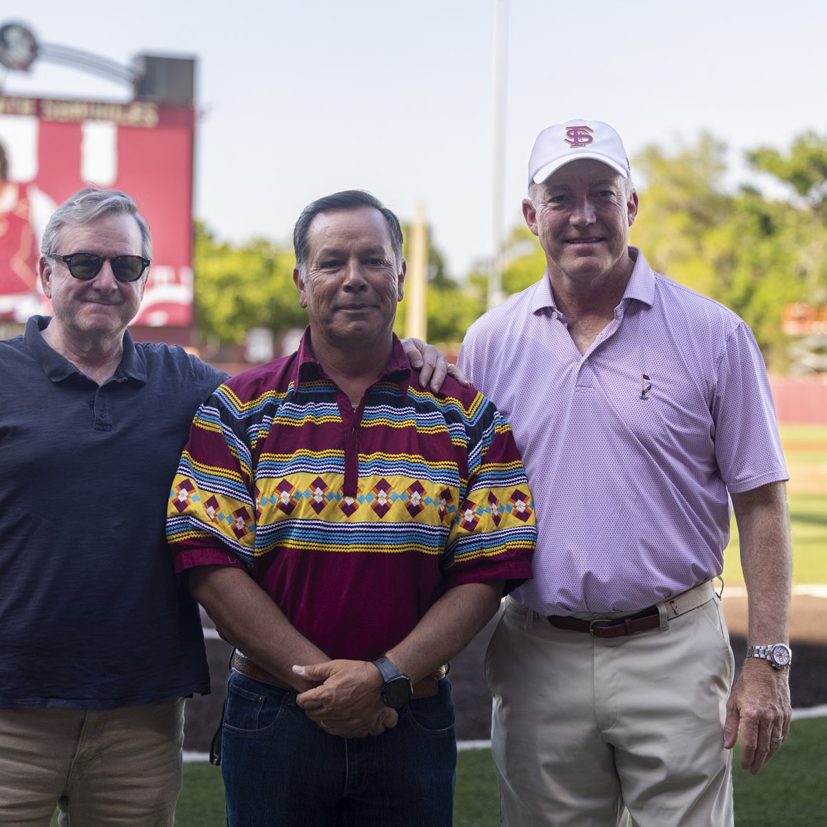 Three men pose for a photo on a baseball field
