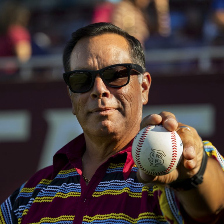 Man wearing sunglasses holds up a baseball