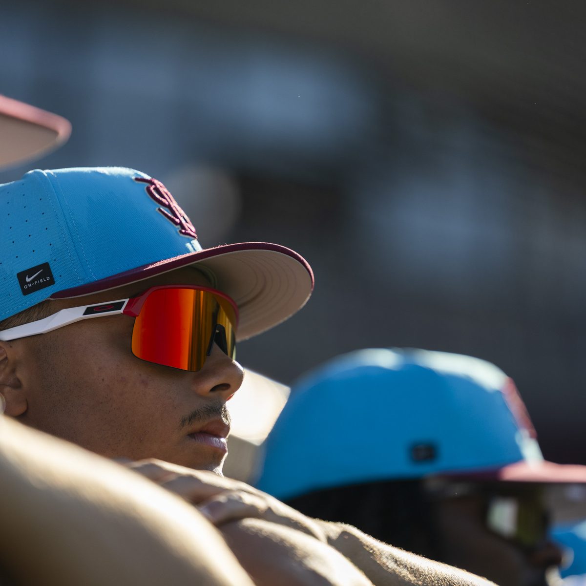 A closeup of a man wearing a blue FSU baseball hate and sunglasses, other people in the background blurred out wearing blue hats