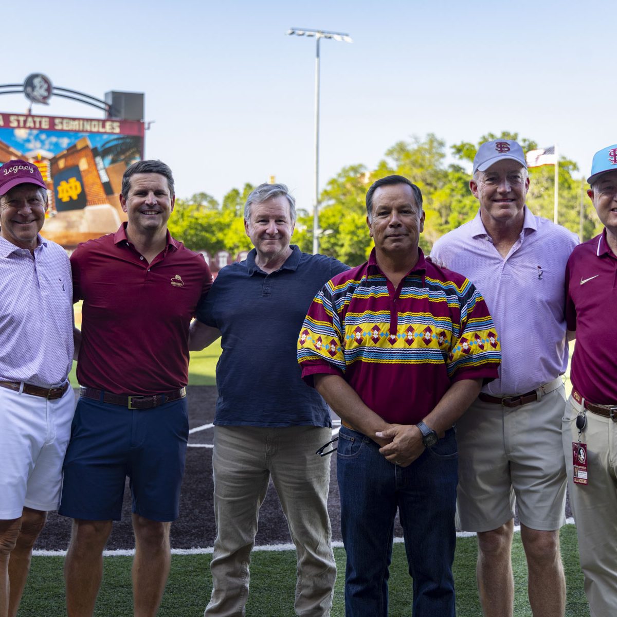 Six men pose for a photo on a baseball field