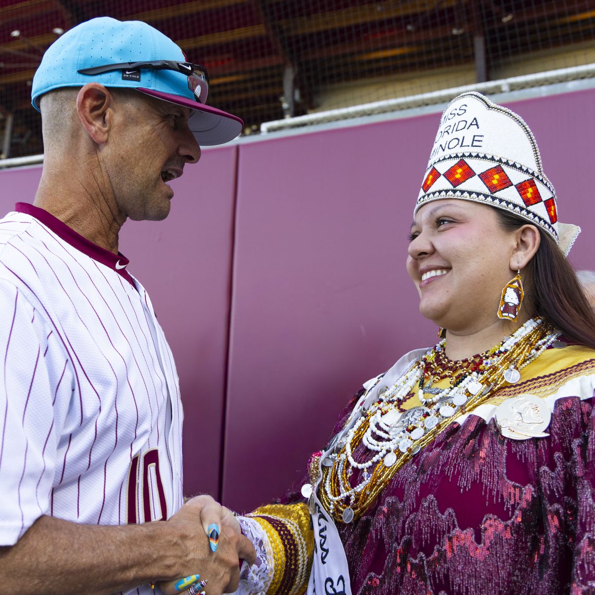 A baseball player shakes a women's hand, the women wears traditional indigenous clothing