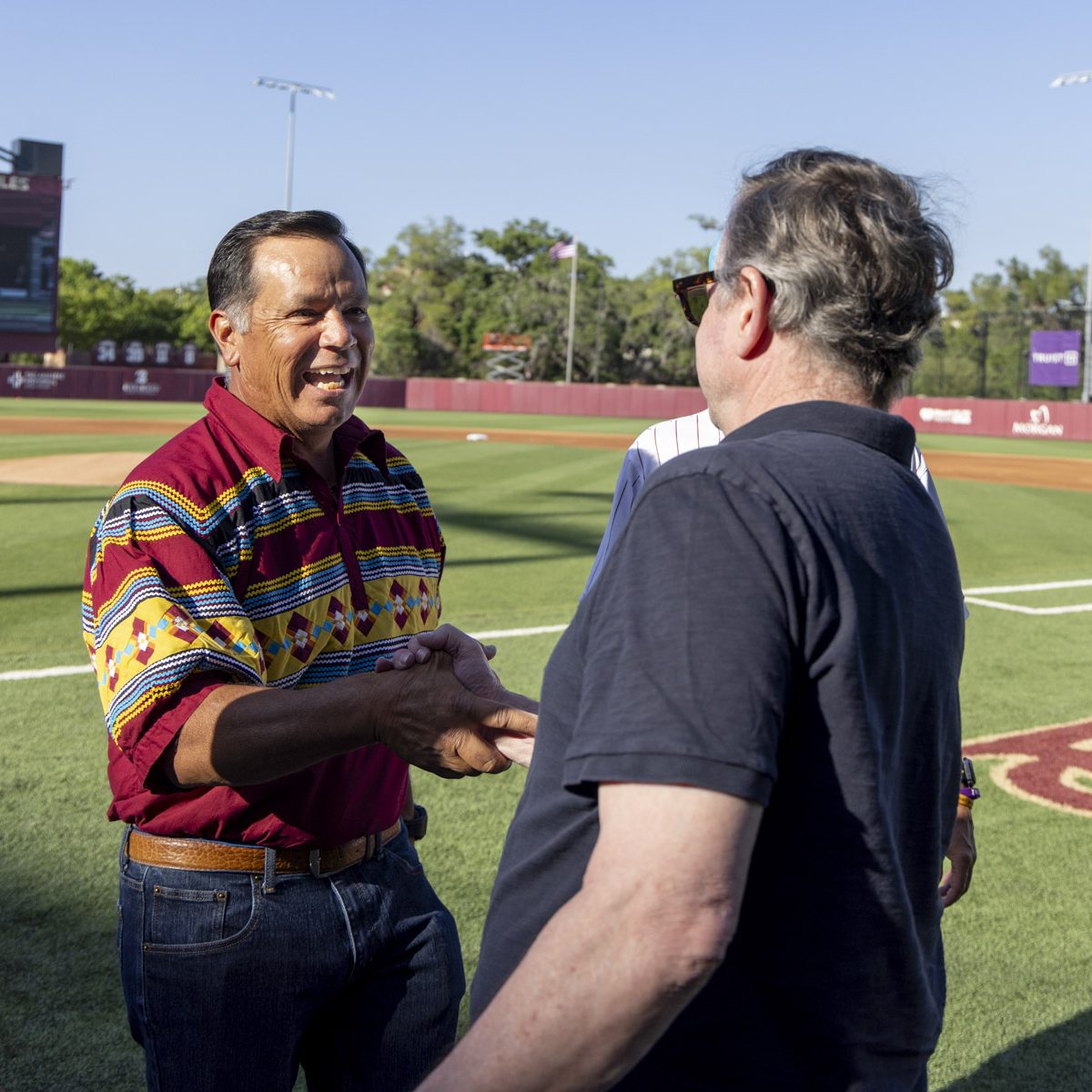 Two men shake hands at a baseball field
