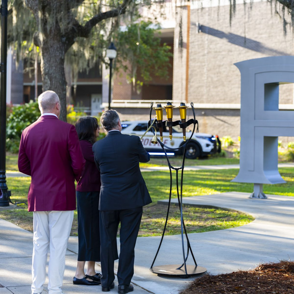 Members of the Florida State Administration stand in front of FSU's ceremonial 3 torches placed out front of the FSU Letters by the student union.