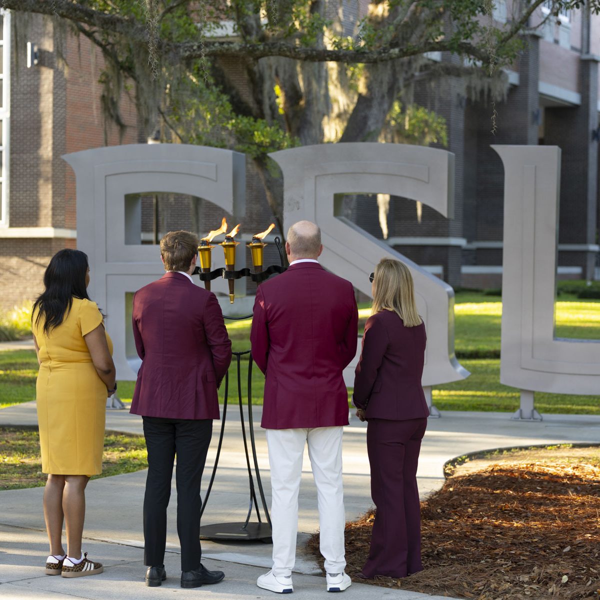 People stand In reflection in front of the FSU ceremonial torches and FSU letters outside the student union.