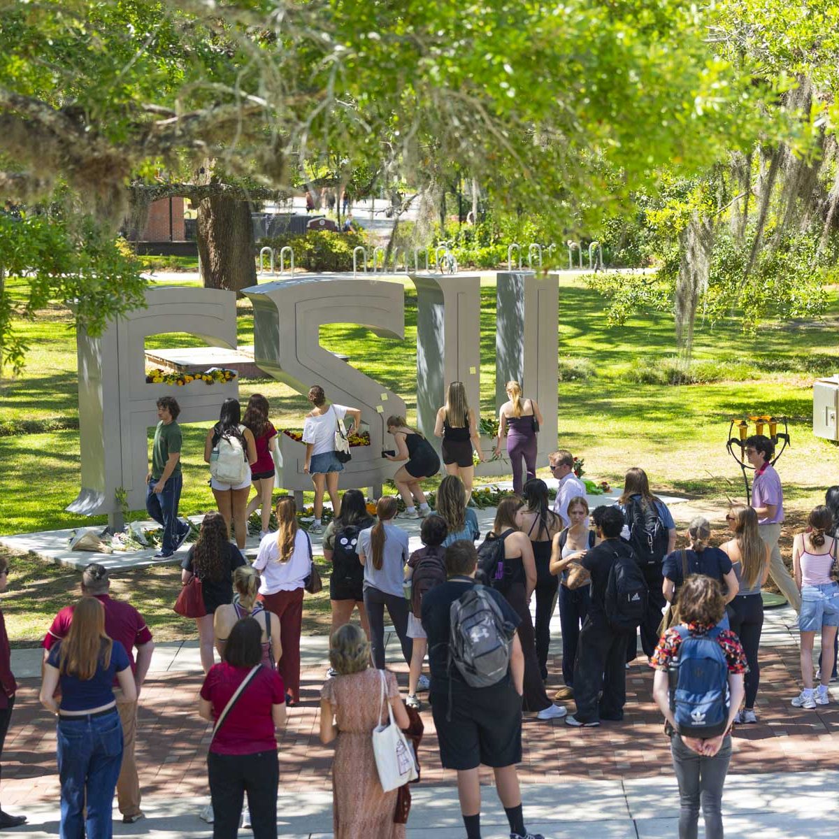 People placing flowers and stand in mourning in front of the FSU letters outside the student union.