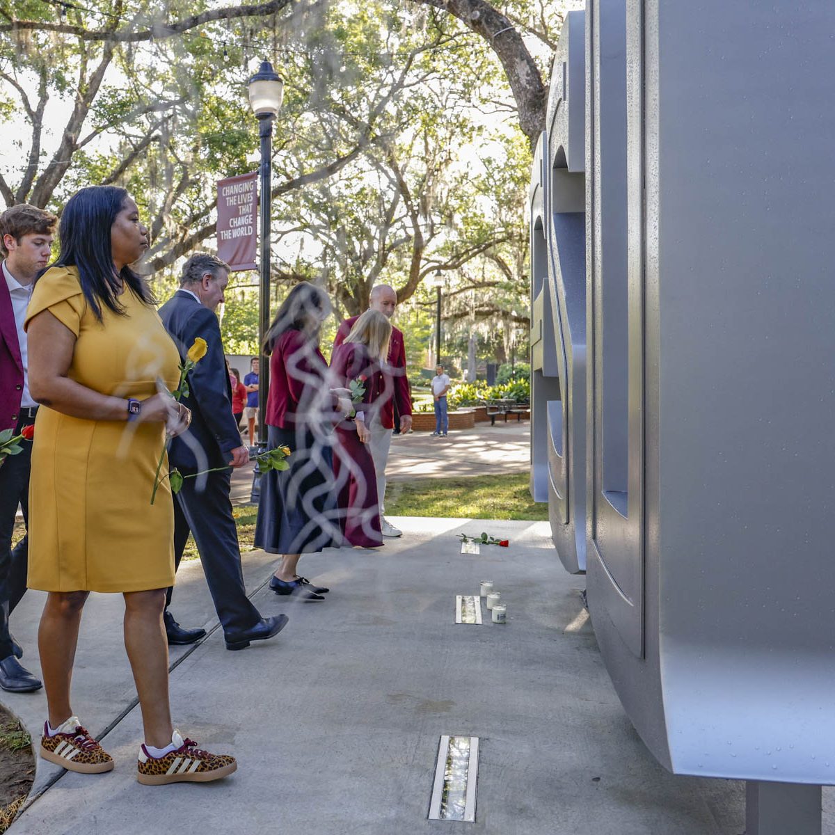 People placing flowers in front of the FSU letters outside the student union.