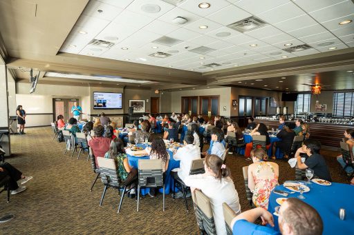 Attendees of the ACC Meeting of the Minds conference sit at tables and listen to a speaker during a closing dinner