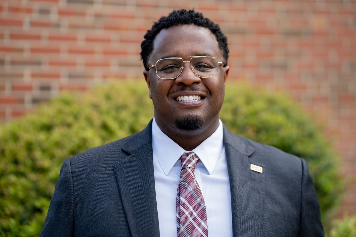 Austin McDonald smiles for a photo in front of a brick wall and bush