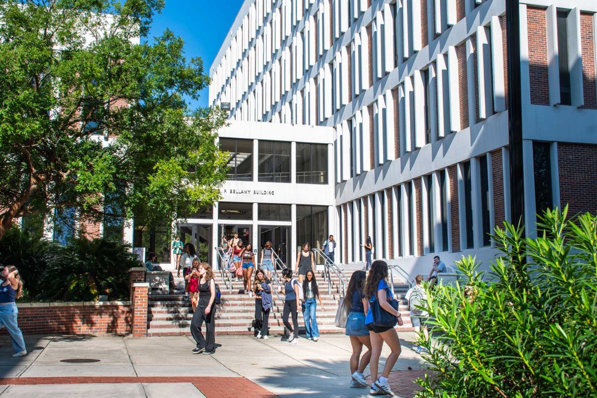 Students walk on the sidewalk and steps of the Bellamy Building, a red brick and white building in the middle of FSU's campus.