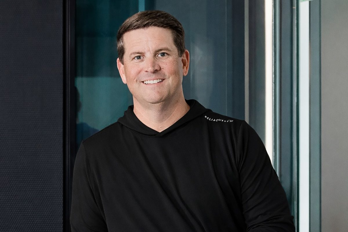 Man in black hoodie posed in front of glass wall.
